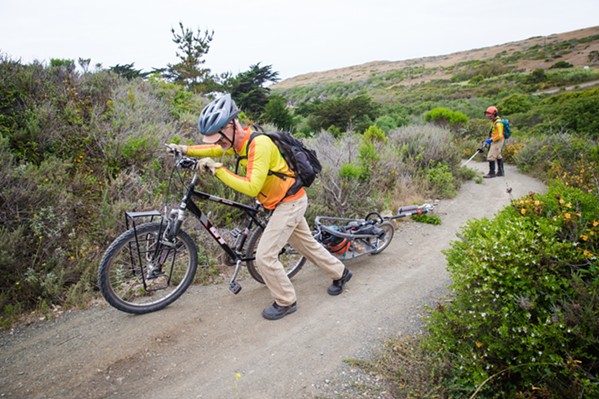 VOLUNTEER WORK Jim Atchison, a volunteer with Central Coast Concerned Mountain Bikers (3CMB), heads up the trail with his brush cutter in tow as Kenny McCarthy clears brush on the trail up to Oats Peak in Monta&ntilde;a de Oro. - PHOTO BY JAYSON MELLOM