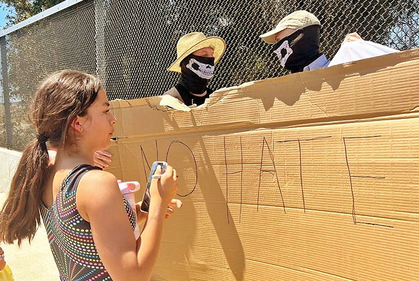 EVERYONE'S INVOLVED A local student writes the phrase "no hate" on the back of a sign being used to block a banner reading "EMBRACE WHITE PRIDE" held up by masked individuals on May 13 in Templeton. - FILE PHOTO COURTESY OF ERIC ALCOSIBA