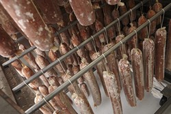 25: :  Inside the drying room, the freshly made salamis are on the racks in the bottom, while the ready to sell versions are hanging above.