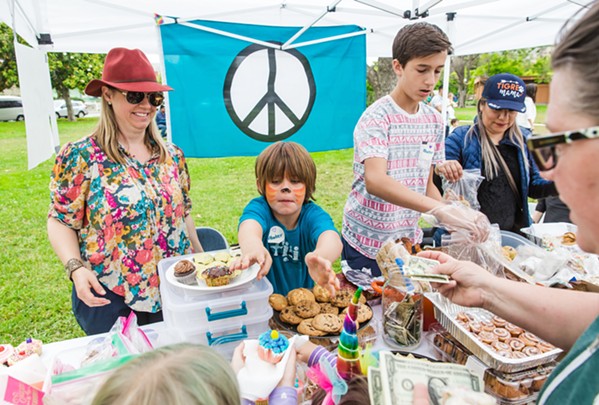 BAKE FOR A CAUSE Ryder Heenan (center), 6, his mother Kristen Heenan (left), and Nathan Durant (right), 14, sell homemade goodies in the Kids for Kids event on June 24 in Mitchell Park. The bake sale raised more than $3,300 for immigrant families who have been separated at the U.S. border. - PHOTO BY JAYSON MELLOM