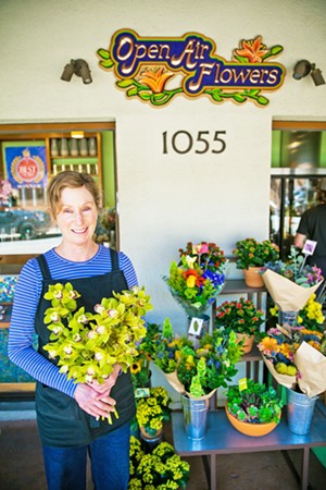 DOWNTOWN FLORA Open Air Flowers has brightened up Osos Street for years with its selection of buds and petals that spill out onto the sidewalk. Owner Leslie Weber holds up a collection of orchids from the display at the Best Flower Shop in the county. - PHOTO BY JAYSON MELLOM
