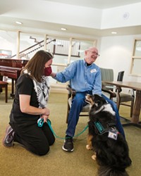 GROUP JOY Alliance of Therapy Dogs volunteer Elise Mebel (left) watches Paul Wilkes of the Wyndham Residence pet her therapy dog, Moosh.