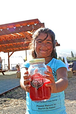 PHOTO BY HAYLEY THOMAS CAIN - FIELD DAY Six-year-old Giuliana Dorado of Julia's Juices celebrates harvest at a rare public City Farm SLO event earlier this month. Behind her, a recently completed pergola offers wind protection for events to come.